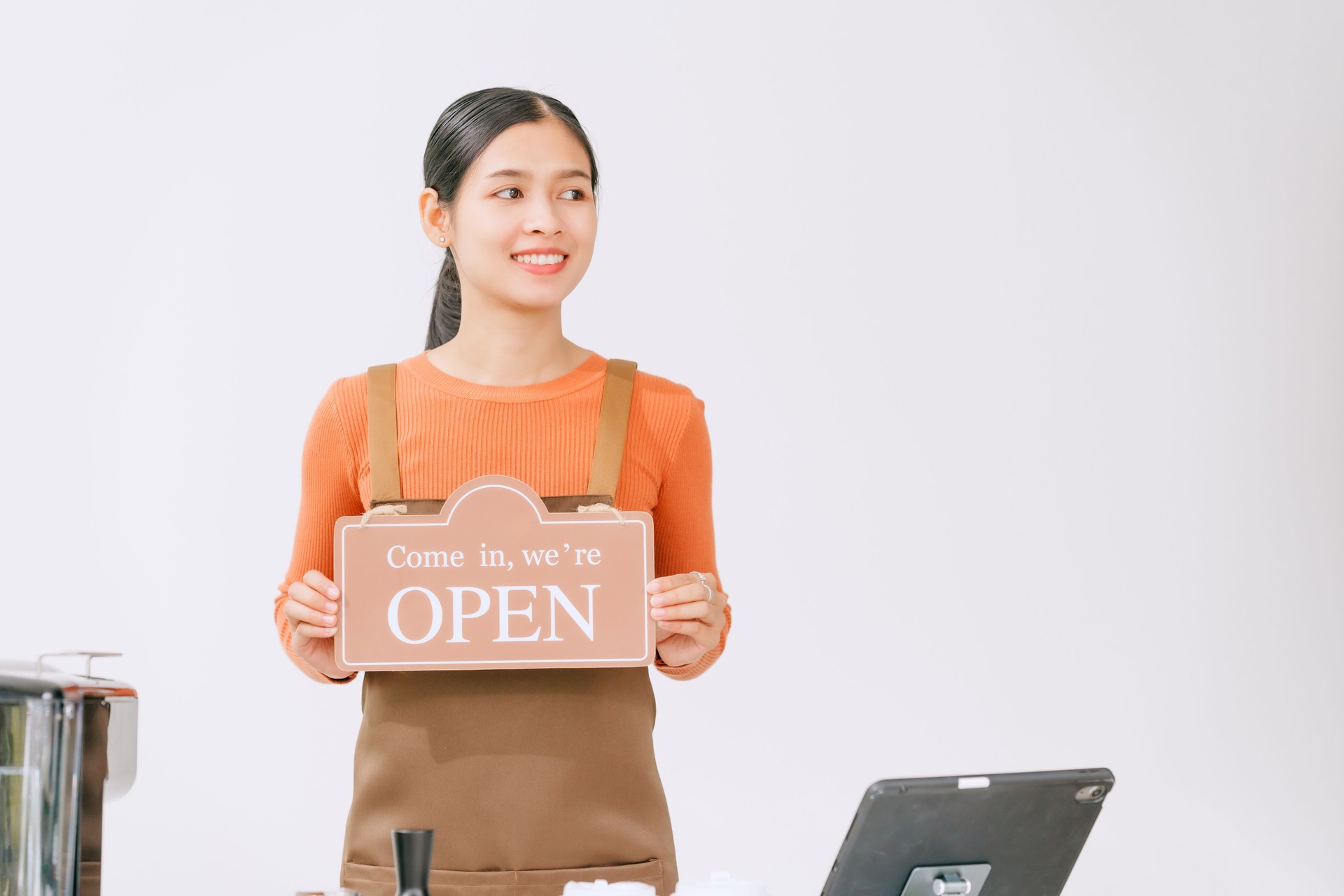 A businesswoman wearing overalls holds an open sign at a coffee shop, welcoming customers with a smile,representing entrepreneurship,hospitality,dedication to providing quality service in her cafÃ©